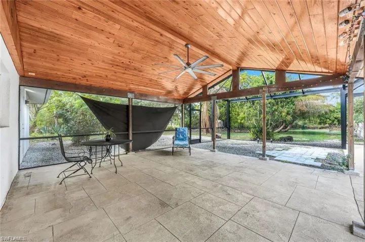 Expansive screened patio featuring a natural wood plank ceiling, exposed wood beams, and a large ceiling fan