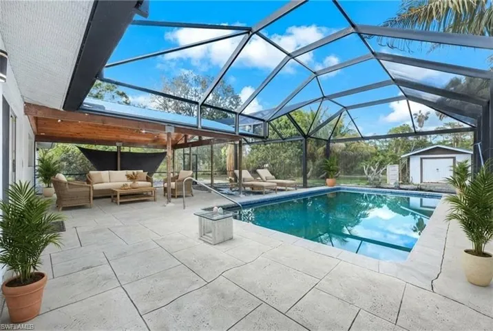 Screened outdoor living area featuring a rectangular swimming pool, spacious paved deck, and an integrated covered patio with a wood-plank ceiling