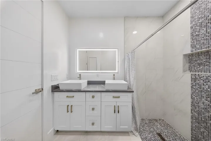 Full bathroom with double vanity and a marble finish shower