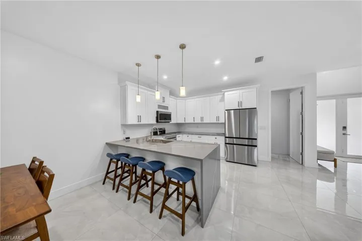 Kitchen featuring a peninsula, stainless steel appliances, white cabinets, dark stone counters, and a kitchen breakfast bar