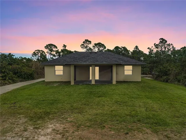 Back of property at dusk with a yard, stucco siding, a sunroom, and roof with shingles