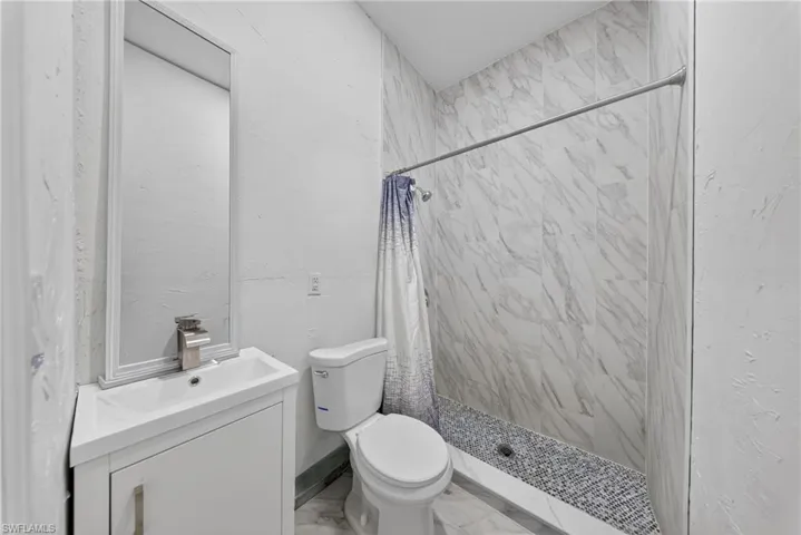 Bathroom featuring vanity, a marble finish shower, and light marble finish flooring