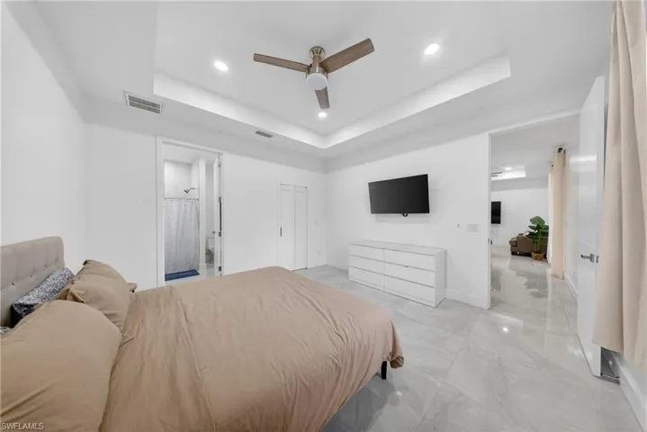 Bedroom featuring recessed lighting, ceiling fan, connected bathroom, a raised ceiling, and light marble finish flooring