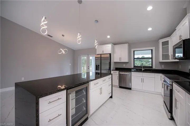 Kitchen featuring light marble finish floors, beverage cooler, appliances with stainless steel finishes, healthy amount of natural light, and recessed lighting