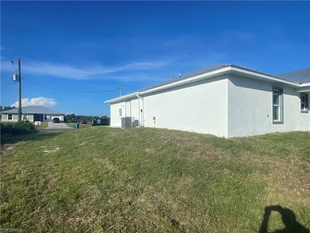 View of side of property featuring stucco siding, a yard, and a metal roof