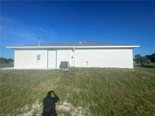 Back of house with a metal roof, stucco siding, and a lawn