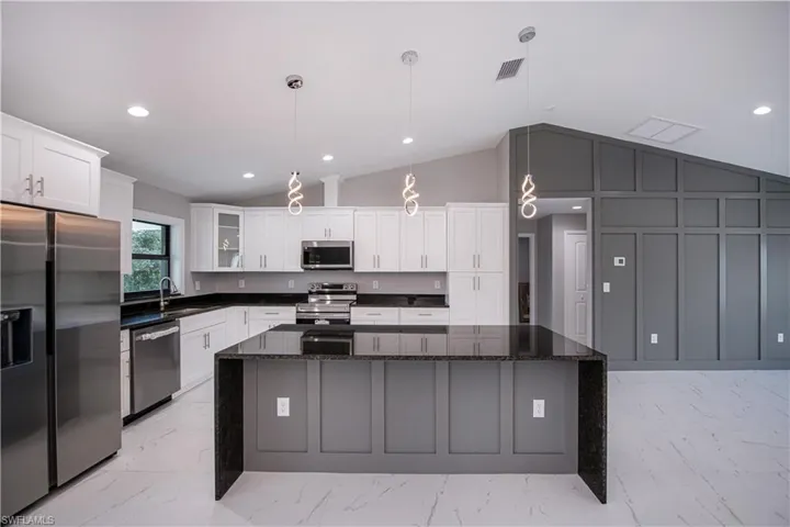 Kitchen with appliances with stainless steel finishes, lofted ceiling, light marble finish floors, recessed lighting, and a center island
