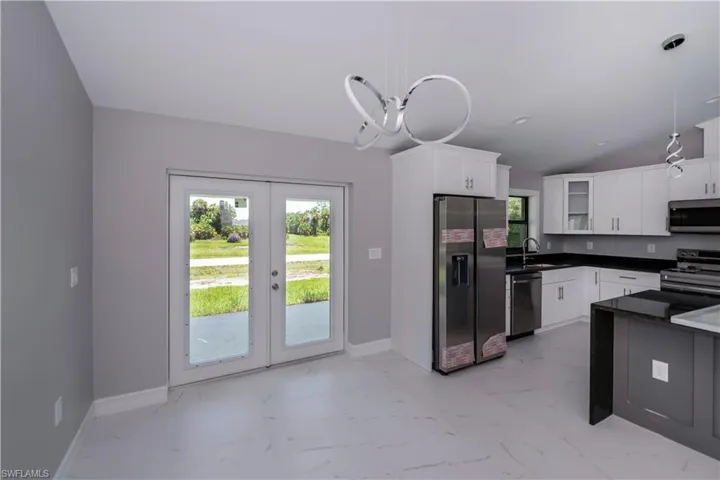 Kitchen featuring stainless steel appliances, light marble finish floors, vaulted ceiling, french doors, and hanging light fixtures