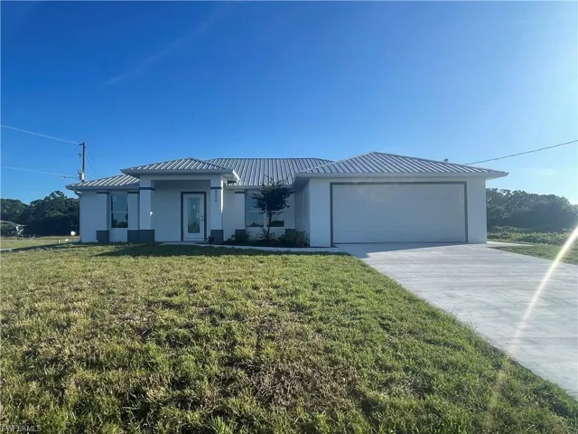 Prairie-style home with stucco siding, concrete driveway, an attached garage, a front lawn, and a metal roof