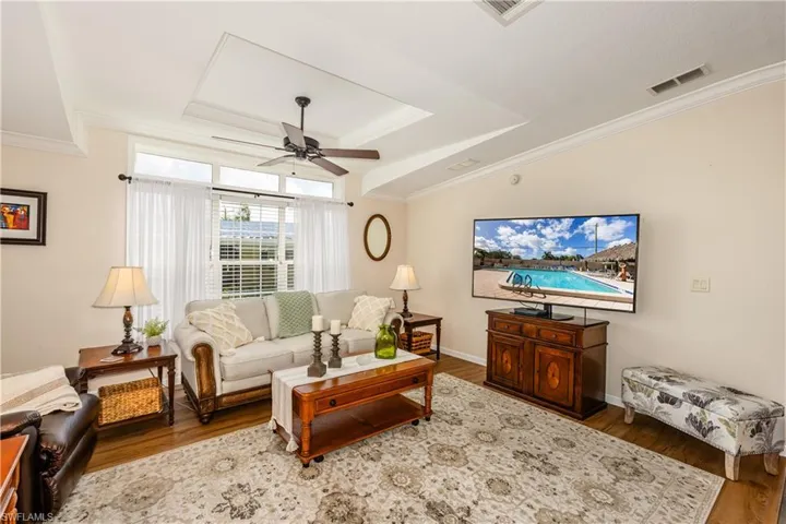 Living area featuring ornamental molding, a ceiling fan, visible vents, a tray ceiling, and wood finished floors