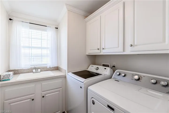 Clothes washing area with a sink, cabinet space, washing machine and dryer, and crown molding