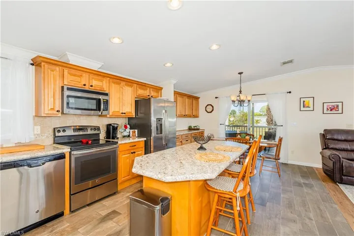 Kitchen with a notable chandelier, ornamental molding, appliances with stainless steel finishes, light wood-style flooring, and decorative backsplash