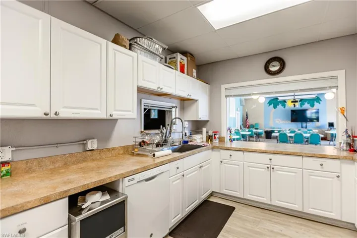 Kitchen featuring light countertops, white cabinetry, white dishwasher, a drop ceiling, and a sink