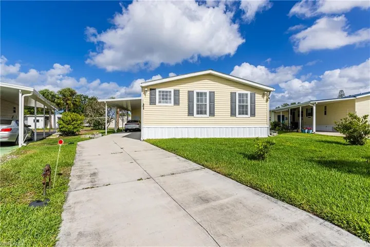 View of front of home featuring concrete driveway, a carport, and a front yard