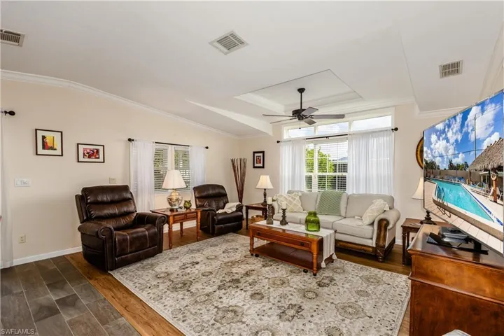 Living room with crown molding, visible vents, ceiling fan, and dark wood-style floors