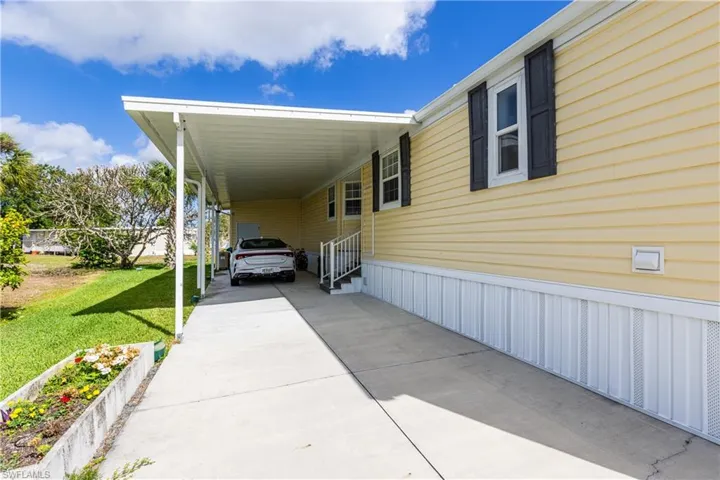 View of side of property featuring a yard, entry steps, an attached carport, and driveway
