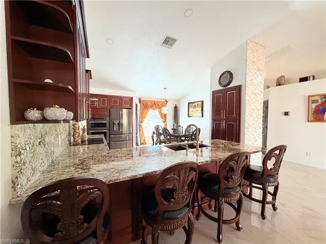Kitchen with a kitchen bar, lofted ceiling, a peninsula, stainless steel appliances, and light stone countertops