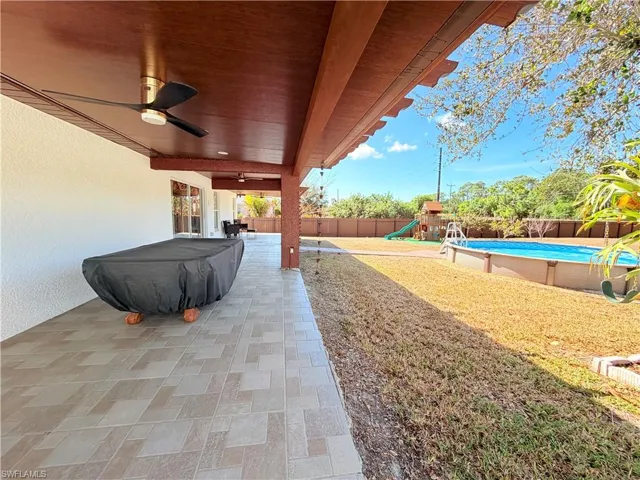 Fenced backyard featuring ceiling fan, a playground, and a patio