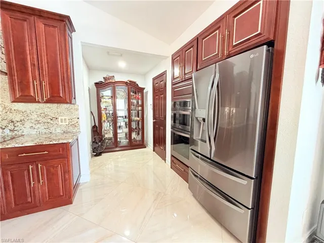 Kitchen featuring stainless steel appliances, bold wood finish cabinets, lofted ceiling, light stone countertops, and tasteful backsplash