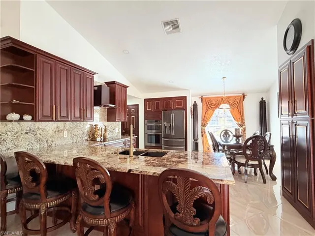 Kitchen with light stone counters, a peninsula, open shelves, stainless steel appliances, and lofted ceiling