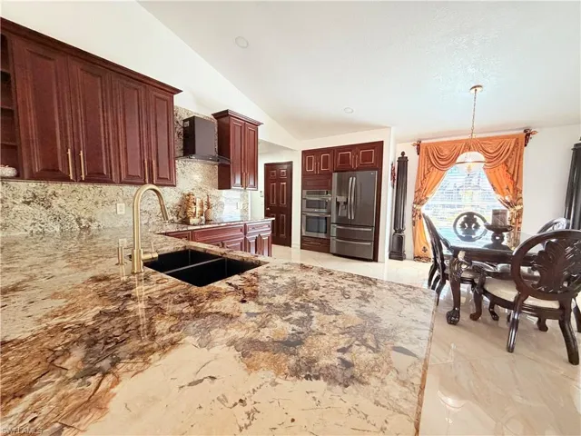 Kitchen with light stone counters, stainless steel appliances, lofted ceiling, tasteful backsplash, and suspended lighting