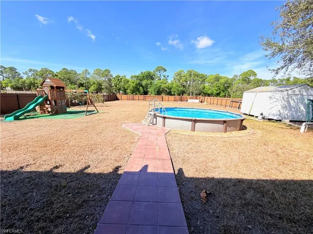 View of pool featuring patio surround, a fenced backyard, a playground, a shed, and view of scattered trees