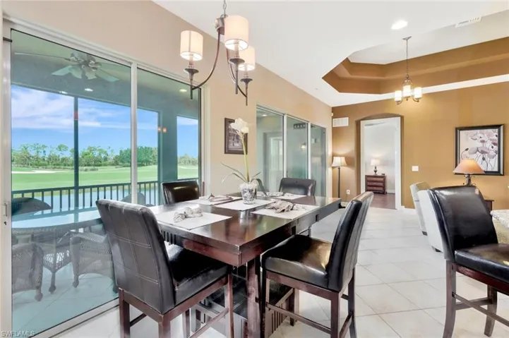 Dining room featuring light tile patterned floors, view of golf course, arched walkways, ceiling fan, and a tray ceiling
