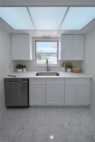 Kitchen with stainless steel dishwasher, white cabinets, and light stone counters