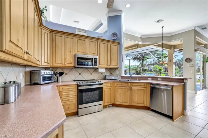 This kitchen is a chef's dream! It has a breakfast bar, sink, stainless steel appliances, pendant lighting, decorative backsplash, and ornamental molding.