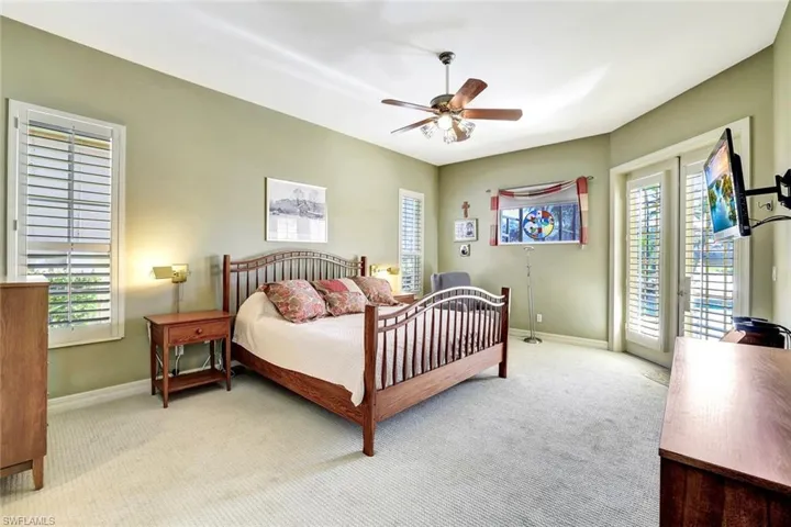 This primary bedroom has a light-colored carpet, a ceiling fan, and french doors that lead to the pool/spa.