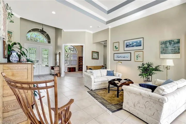 Living room featuring double entry doors, light tiled floors, crown molding, and a high ceiling