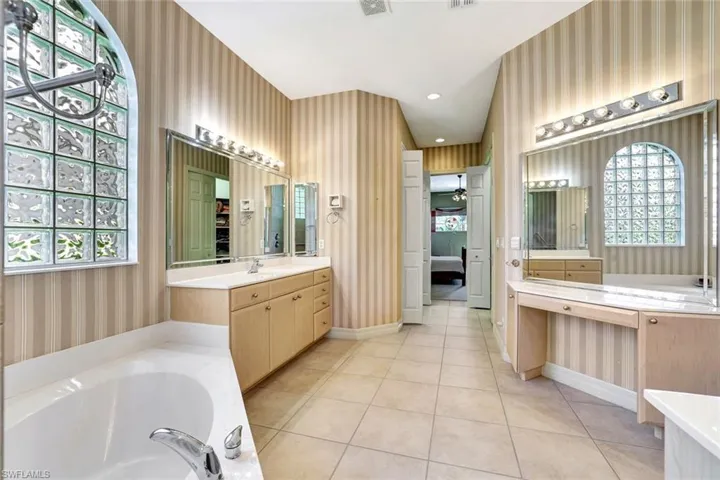 Primary bathroom has vanities with built-in sinks and storage space. Tile flooring, bathtub and a shower with multiple showerheads.