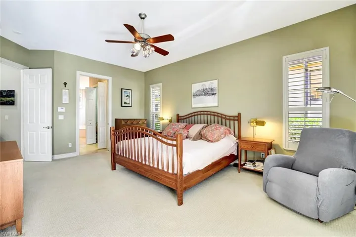 This primary bedroom has an en suite bathroom. The bedroom has a light-colored carpet, a ceiling fan, and french doors that lead to the pool and spa.