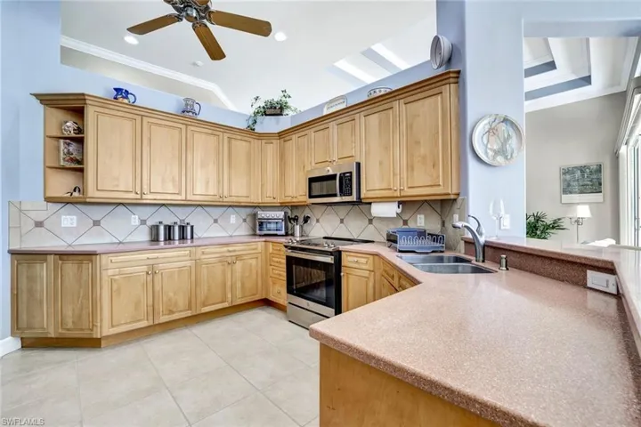 This kitchen has a tile backsplash, stainless steel appliances, and ornamental molding. It also has a double sink.