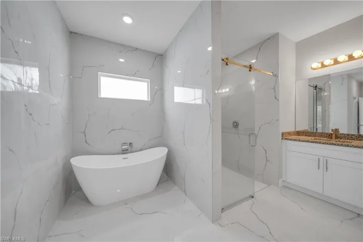Bathroom with stone wall, a marble finish shower, a freestanding bath, vanity, and recessed lighting