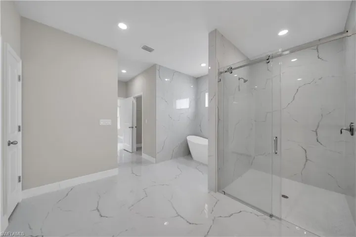 Full bath with a freestanding bath, a marble finish shower, recessed lighting, and stone wall