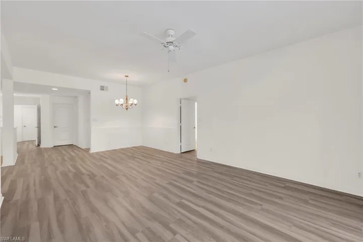 Empty room with a ceiling fan, a chandelier, and light wood-style floors