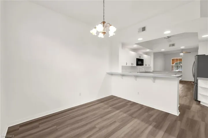 Kitchen featuring a peninsula, dark wood-style floors, a breakfast bar area, freestanding refrigerator, and a chandelier