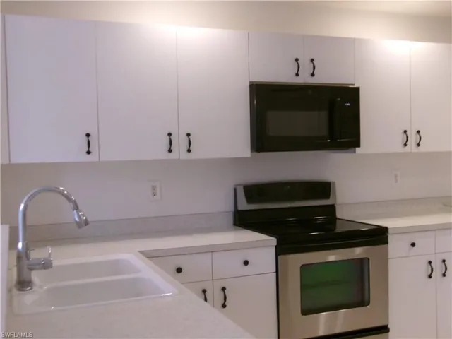 Kitchen with black microwave, electric stove, a sink, and light countertops
