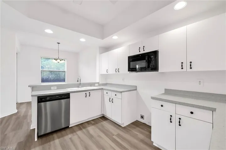 Kitchen with recessed lighting, light wood-style floors, stainless steel dishwasher, black microwave, and light countertops