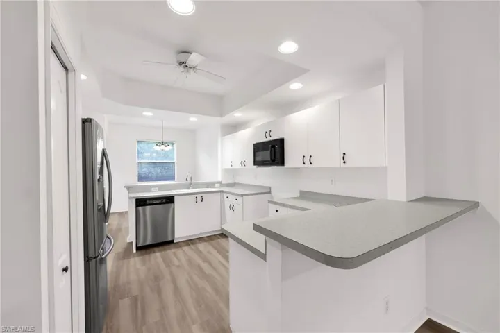 Kitchen with a peninsula, a ceiling fan, light wood finished floors, stainless steel appliances, and white cabinetry