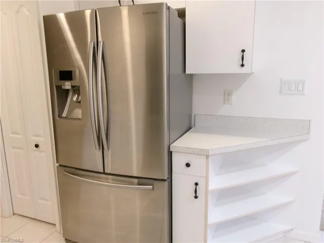 Kitchen with stainless steel fridge with ice dispenser, light countertops, white cabinets, open shelves, and light tile patterned flooring