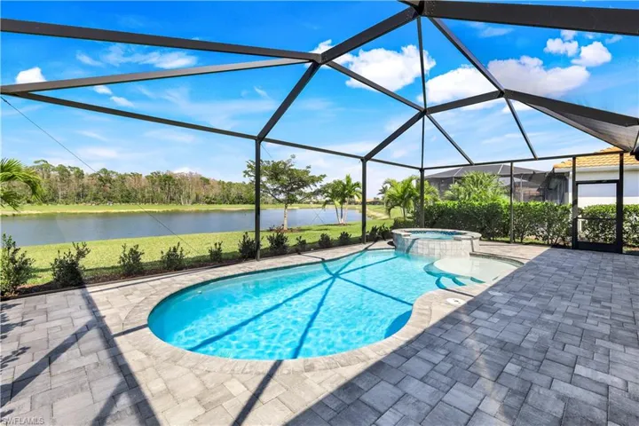 View of swimming pool featuring a patio, a pool with connected hot tub, a water view, a lawn, and a lanai
