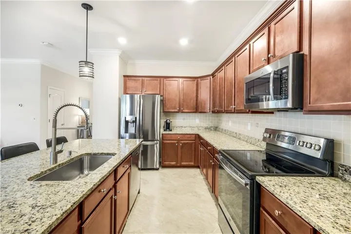 Kitchen featuring decorative backsplash, stainless steel appliances, crown molding, pendant lighting, and a sink
