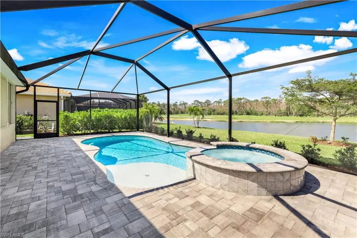View of pool featuring a patio, glass enclosure, a water view, and a pool with connected hot tub