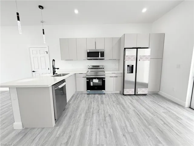 Kitchen with pendant lighting, sink, appliances with stainless steel finishes, gray cabinetry, and light wood-type flooring