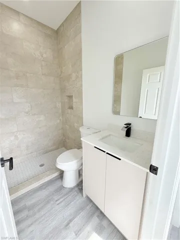 Bathroom with vanity, wood-type flooring, toilet, and tiled shower