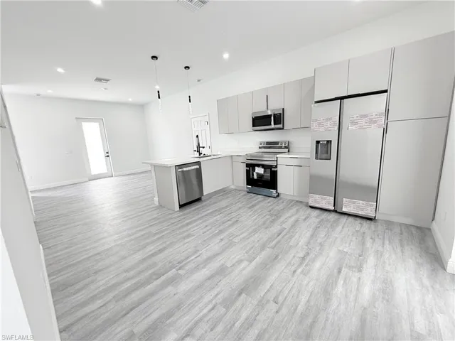 Kitchen featuring gray cabinetry, decorative light fixtures, appliances with stainless steel finishes, kitchen peninsula, and light hardwood / wood-style floors