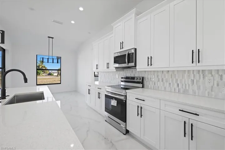 Kitchen featuring stainless steel appliances, white cabinets, quartz countertops, recessed lighting, and decorative light fixtures