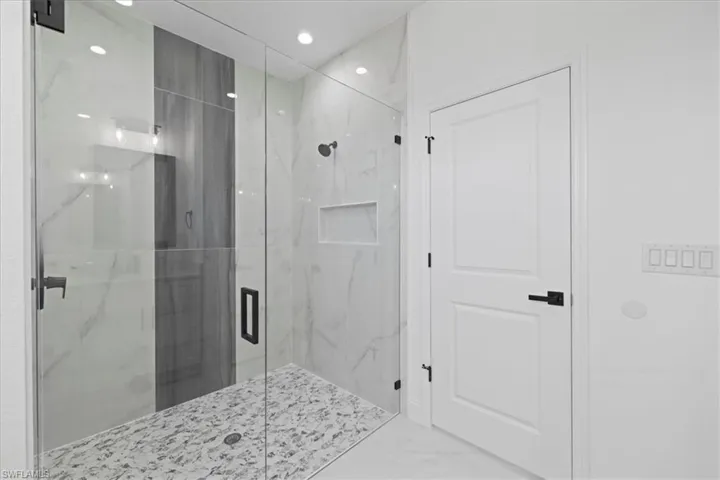 Full bathroom shower, marble look tiles, and recessed lighting